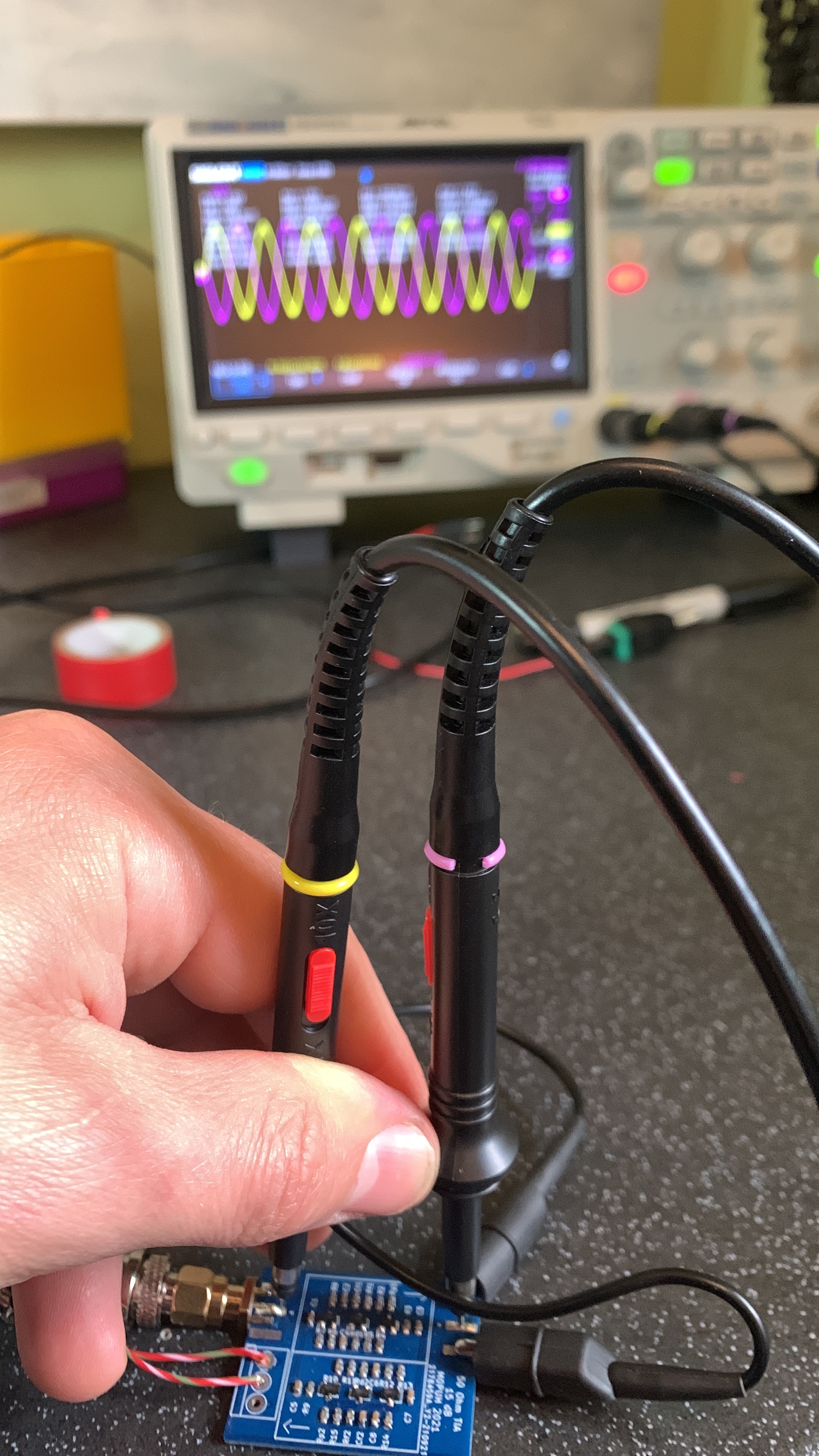 A circuit board being tested with an oscilloscope in the background