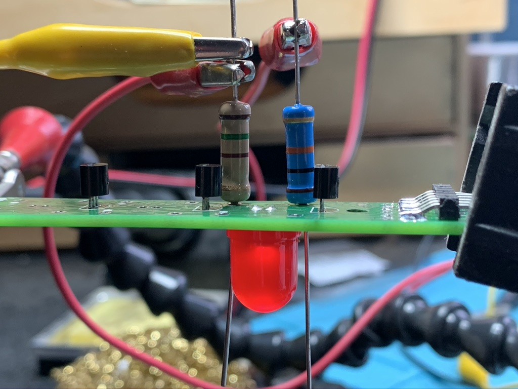 The same PCB from the side. There’s a large LED on the bottom of the board and two resistors on the top. The resistors are connected with crocodile clips (to the positive supply rail which is not shown).