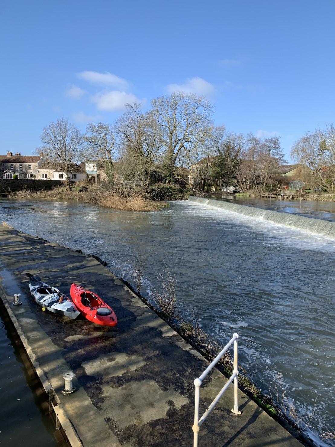 Two kayaks on a concrete bar. There is a weird on the right and fast moving water in front of the weir. 