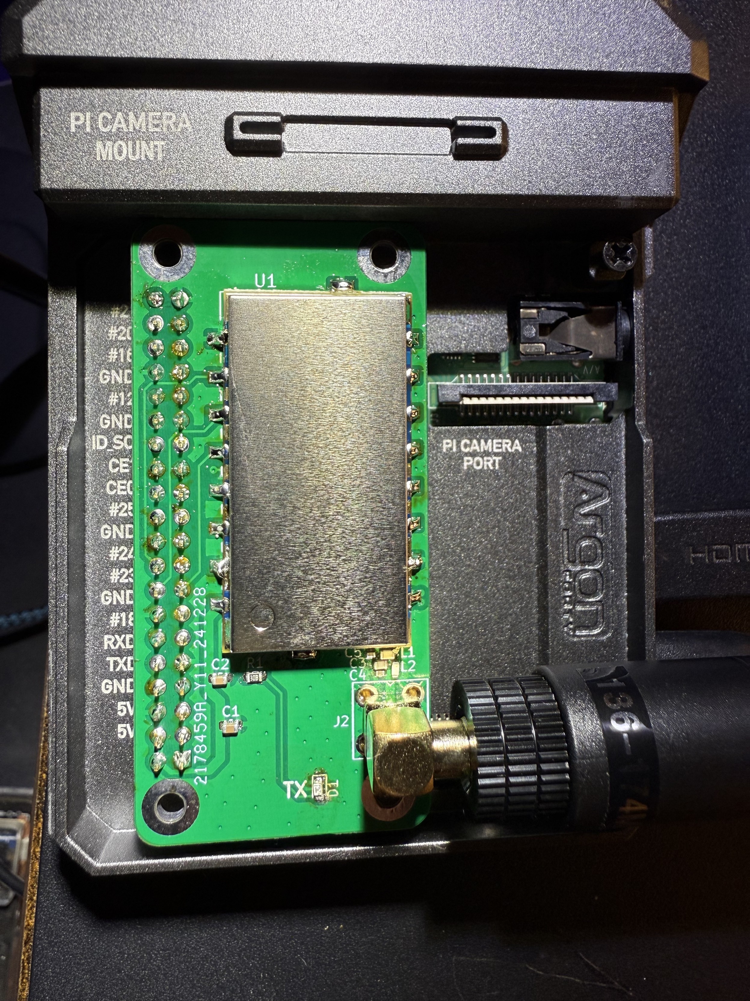 A metal raspberry pi case showing a hat circuit. It’s a metal rectangle, oriented vertically, on the right and a row of headers on the left. An antenna is connected on the bottom right